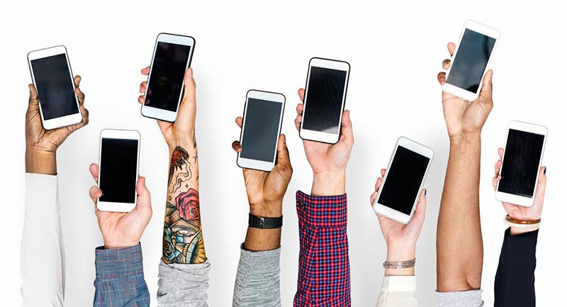 8 different people's hands holding smart phones up in the air